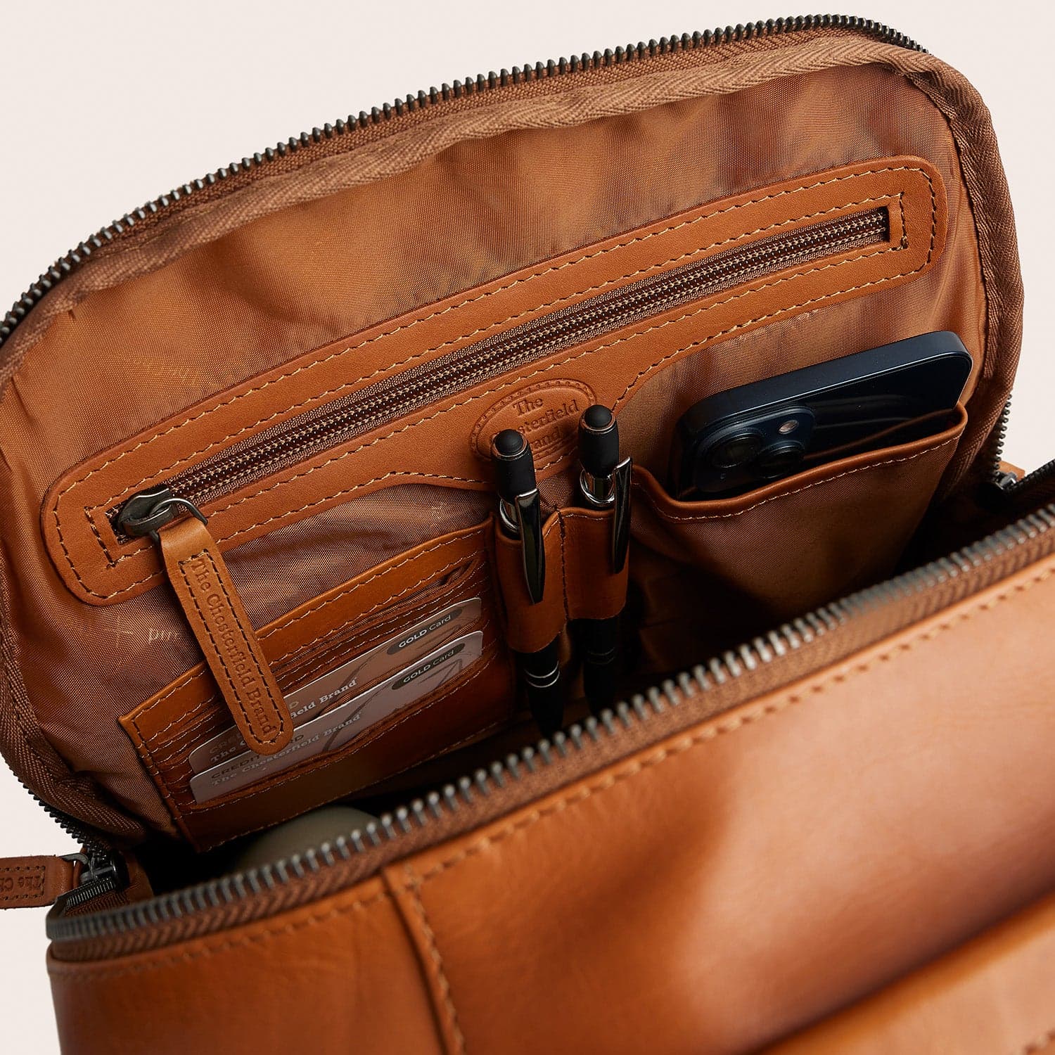Interior of a cognac leather backpack with a phone pocket, pen holders, card slots and a zipped compartment