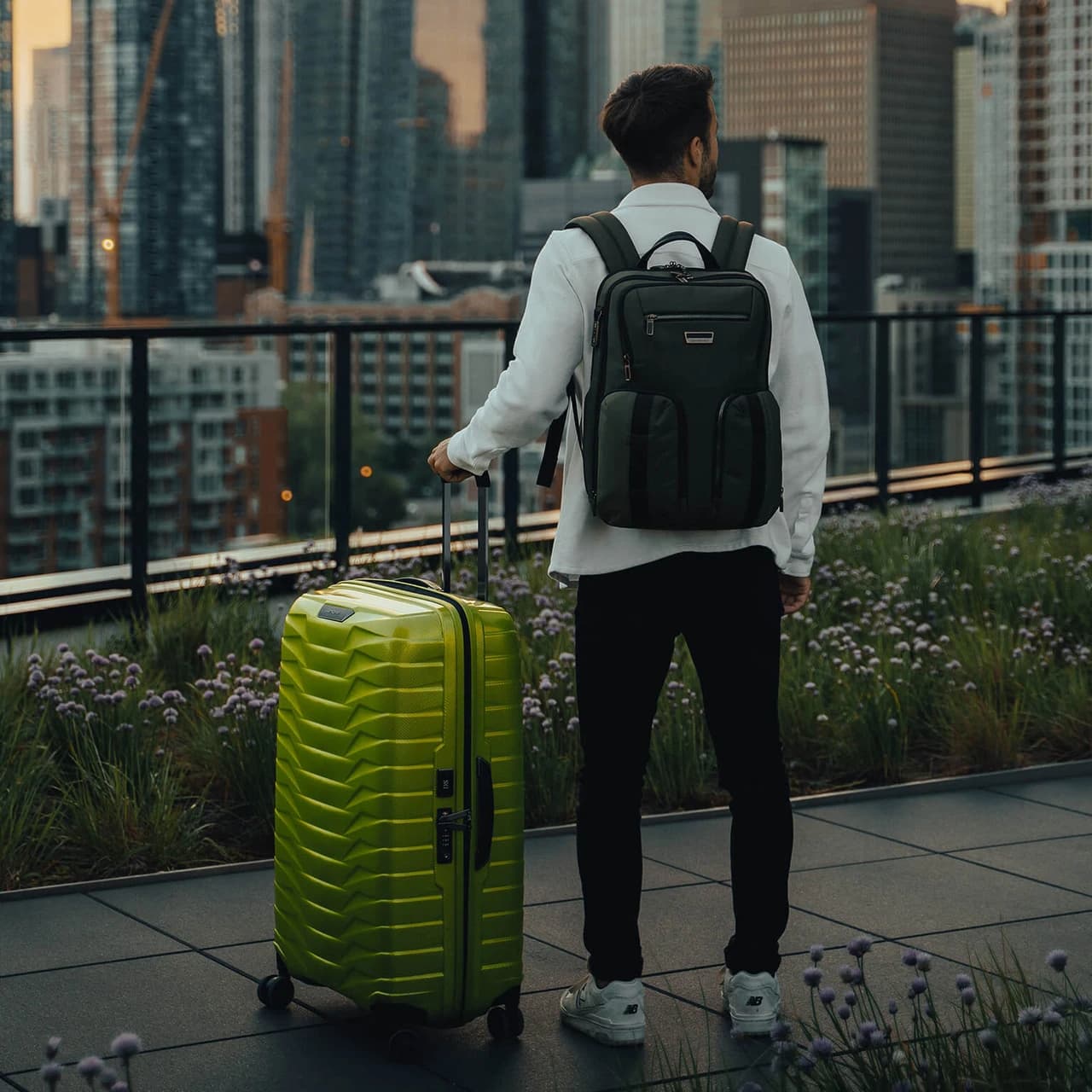 Reisender mit schwarzem Rucksack und limettengrünem Samsonite Koffer vor einer Skyline