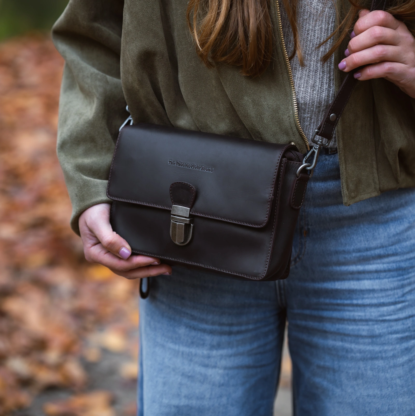 Brown Chesterfield Lucca shoulder bag with a metal clasp, worn with jeans and a green jacket