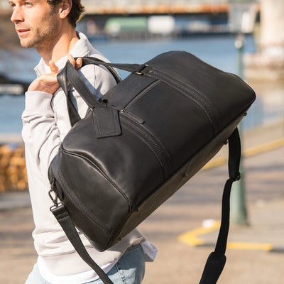 Man carrying a black Chesterfield Rivaro weekend bag over his shoulder by the water
